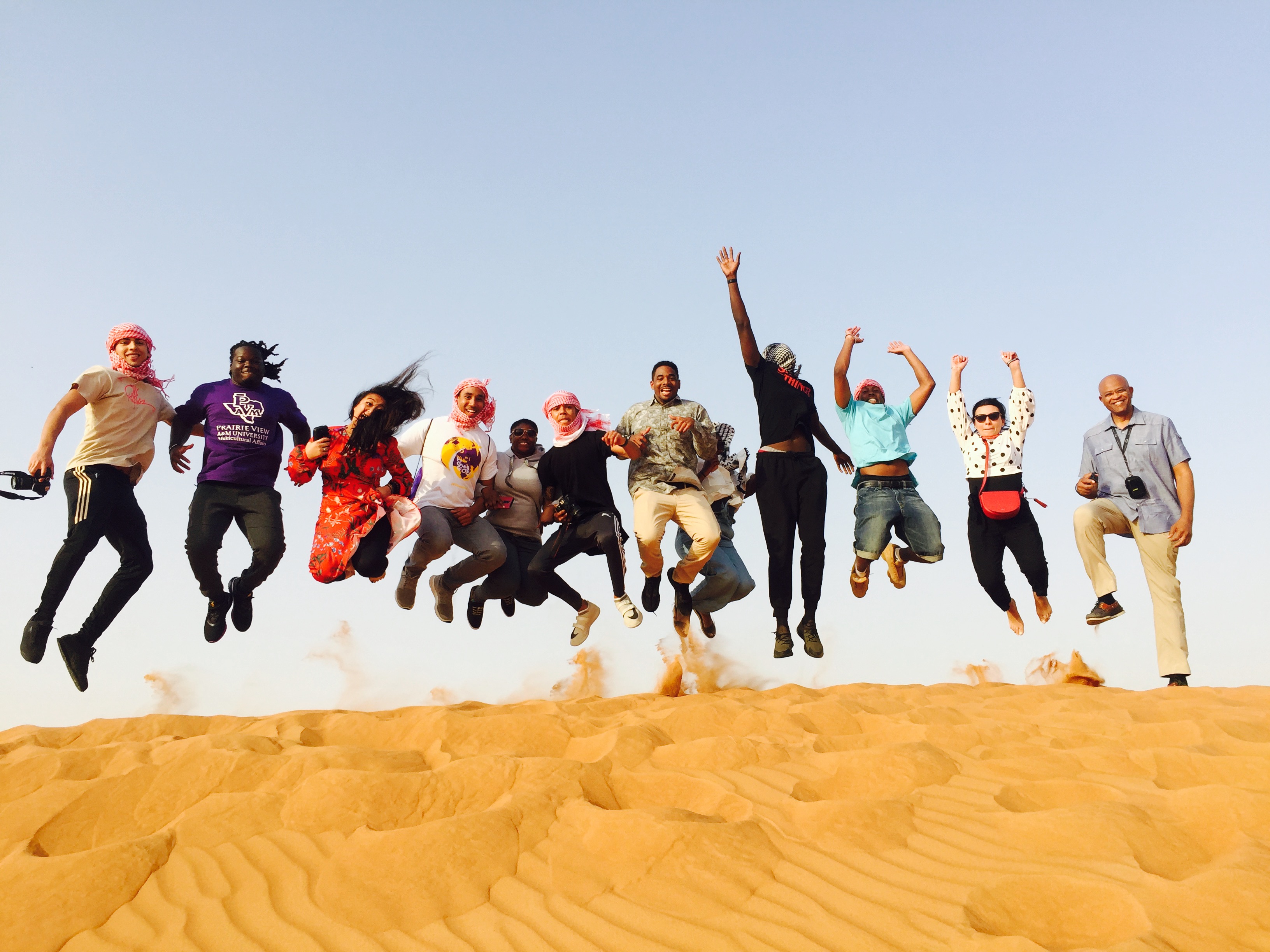 PVAMU students leap in the air above a sand dunes in Dubai