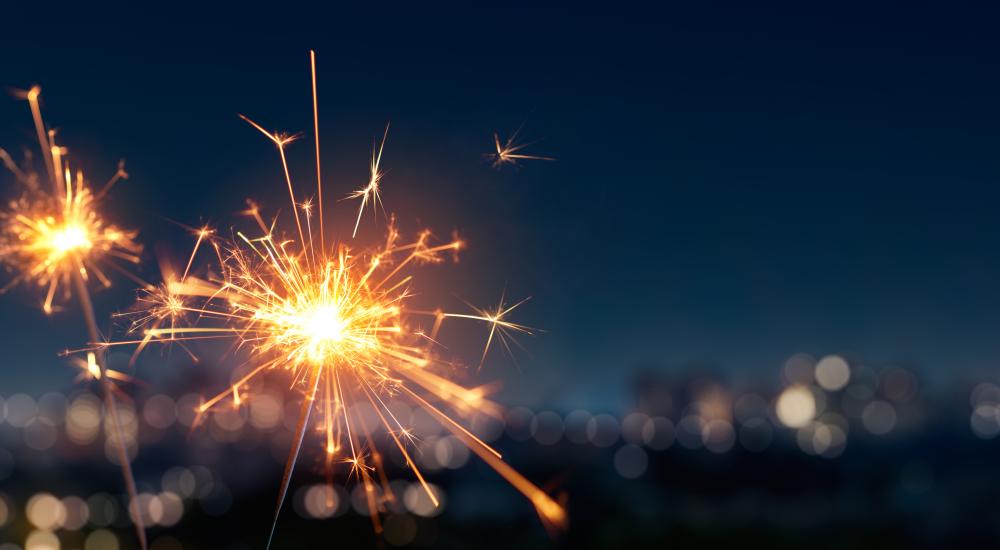 Two sparklers lit with a city skyline in the background