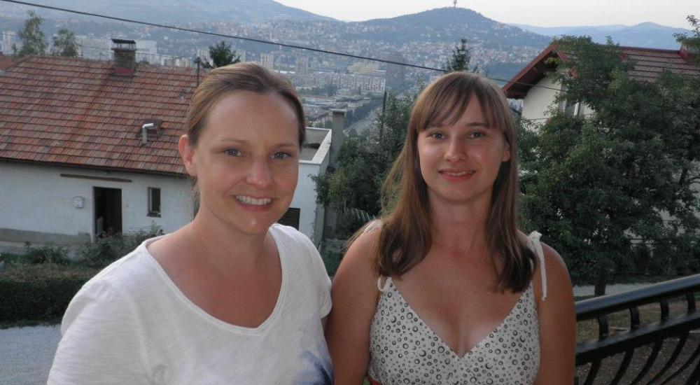 Two women smile on a balcony overlooking a town in Bosnia and Herzegovina