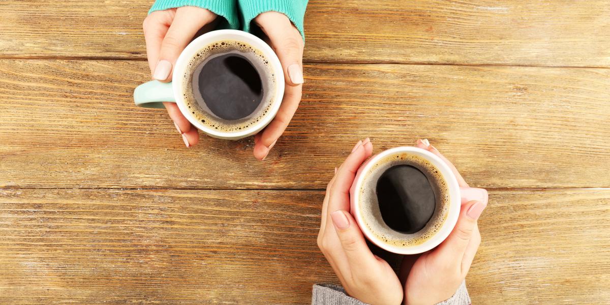 Two people holding cups of coffee on a table