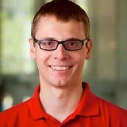 Headshot of Josh Whitson. Josh is wearing glasses and an orange t-shirt. 