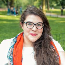 Hannah Thomas, seated outside wearing a white shirt and an orange scarf