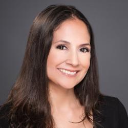 Woman with long dark hair, and brown eyes, against a dark grey background