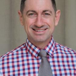 Morgan smiles in a red and white checkered shirt with gray tie