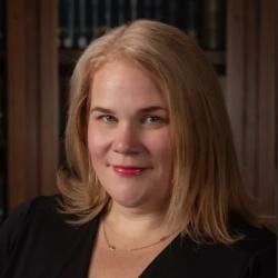 Jennifer smiles, wearing a black top in front of a bookshelf