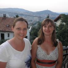 Two women smile on a balcony overlooking a town in Bosnia and Herzegovina