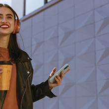 young smiling woman in headphones holding coffee and phone